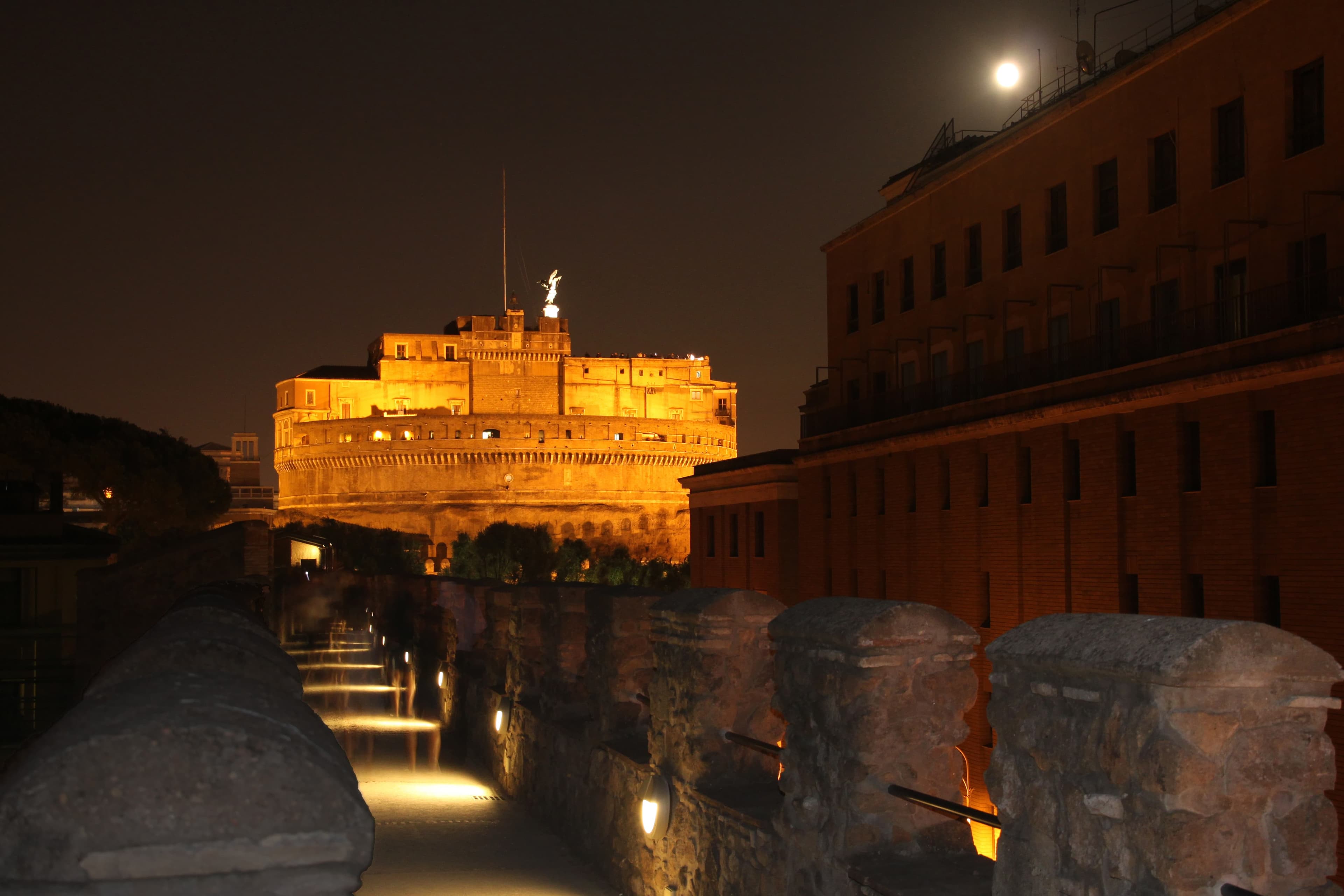 Night view of the Passetto di Borgo in the direction of Castel Sant'Angelo, the fortified corridor lit against the dark Roman sky