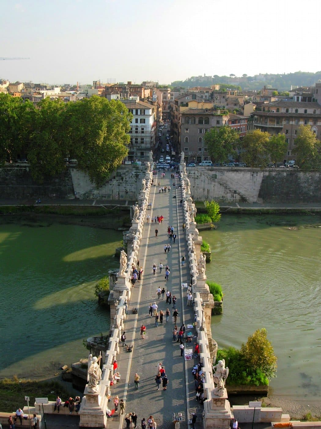 Aerial view of Ponte Sant'Angelo from above, showing the full bridge with Bernini's ten angel statues lining both sides, pedestrians crossing, and the historic centre of Rome in the background