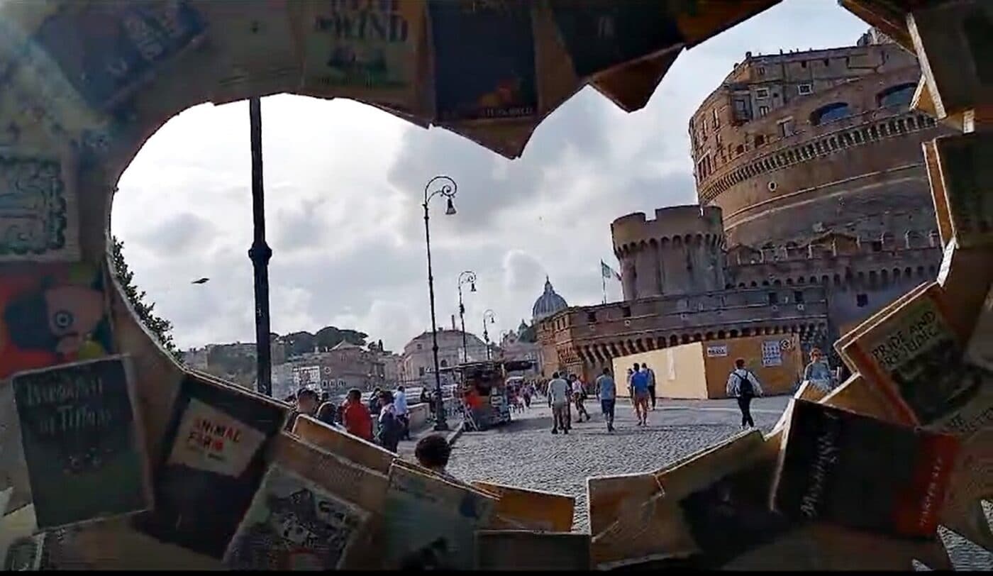 Books frame the view of Castel Sant'Angelo from inside Biblio Bar Roma — open-air library and bar on Lungotevere Castello