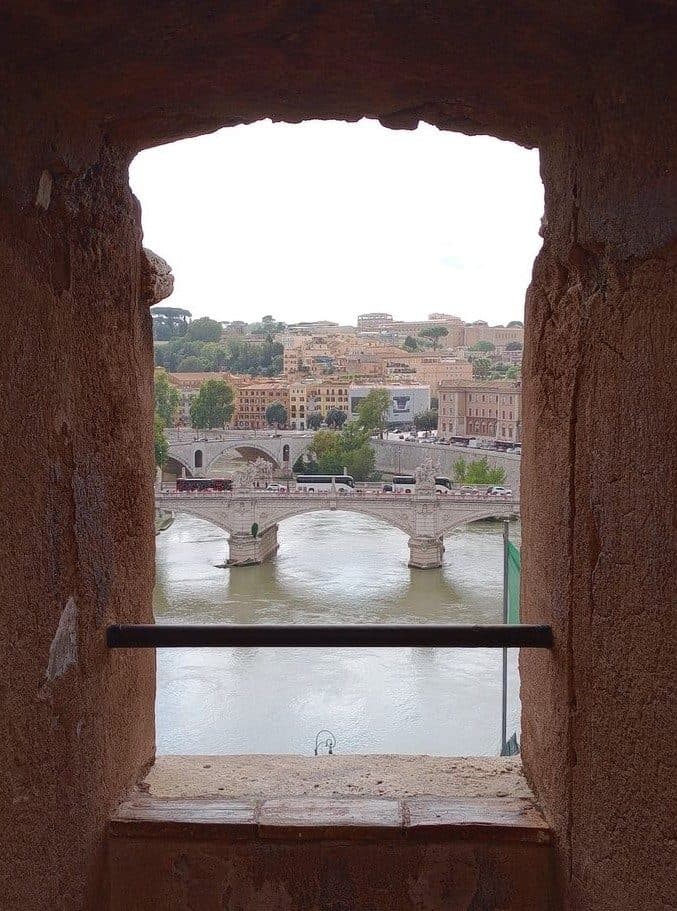 Ponte Vittorio Emanuele II seen from a stone embrasure in the Bastioni of Castel Sant'Angelo, with the Tiber river and the Janiculum hill visible beyond