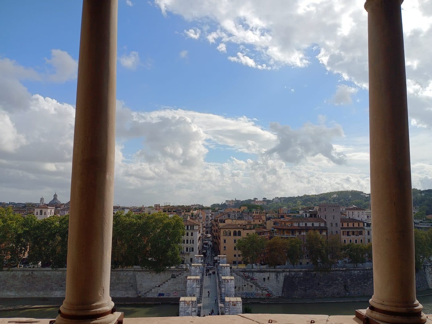 Ponte Sant'Angelo seen from inside Castel Sant'Angelo, framed between the columns of the Loggia di Giulio II, with the bridge under restoration scaffolding for the 2025 Jubilee