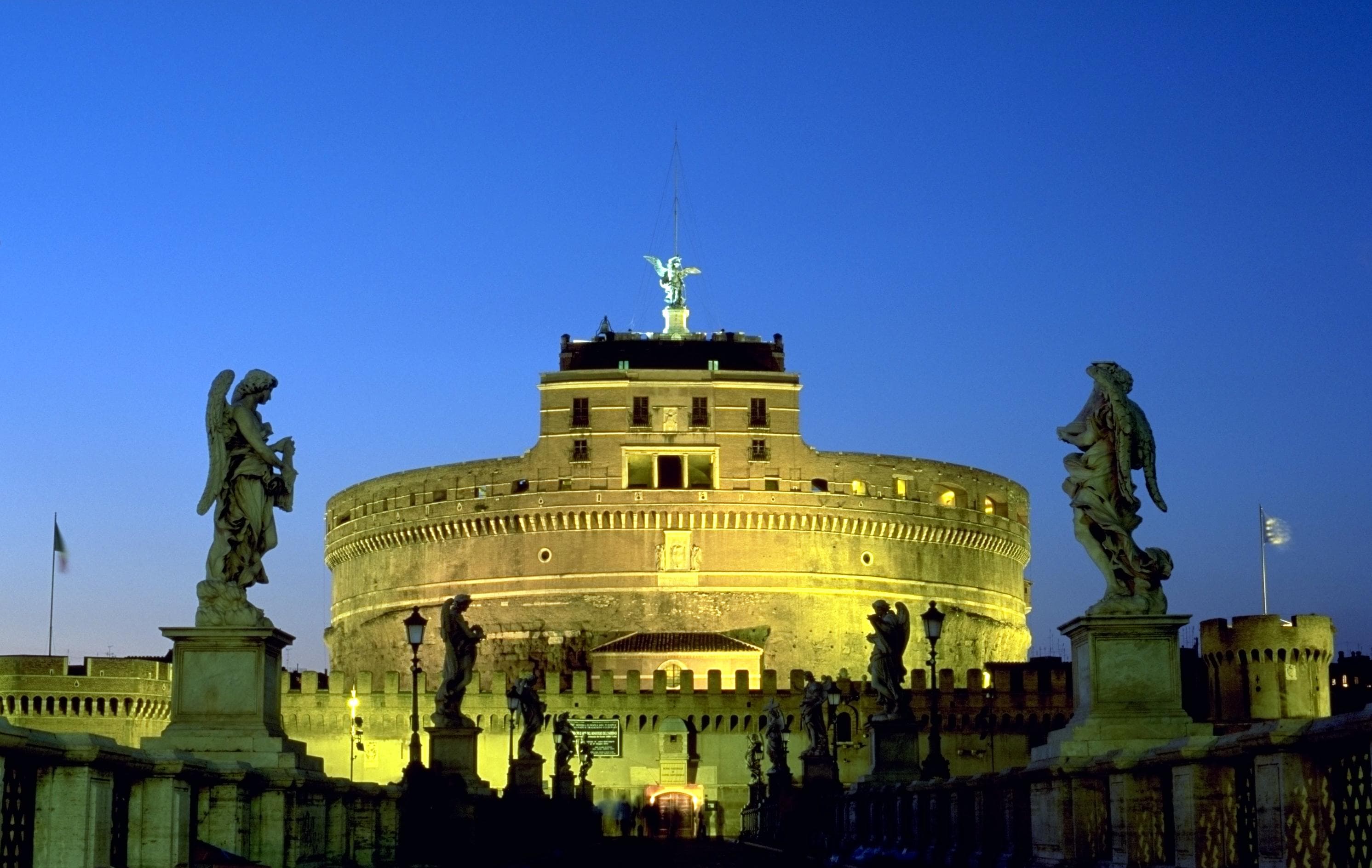 Castel Sant'Angelo in Rome seen from the Tiber embankment during daytime, with Ponte Sant'Angelo and Bernini's angel statues visible in the foreground
